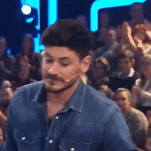 A Man With A Beard And Mustache Is Standing In Front Of A Crowd Of People GIF