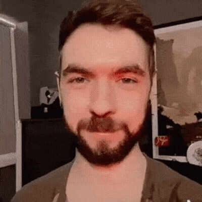 A Man With A Beard And Mustache Is Standing In Front Of A Framed Picture . GIF