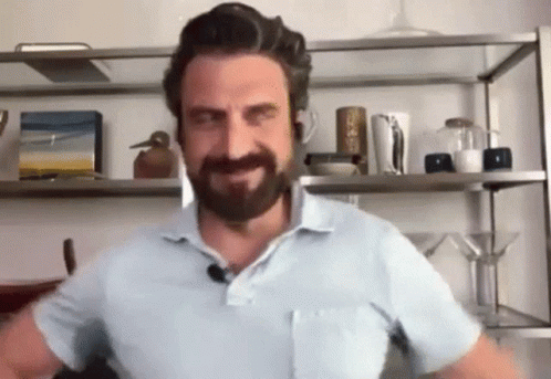 A Man With A Beard And Mustache Is Standing In Front Of A Shelf In A Room . GIF