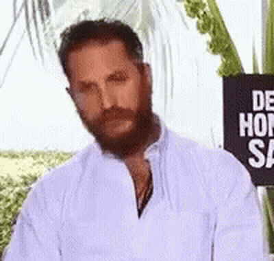 A Man With A Beard And Mustache Is Standing In Front Of A Sign That Says `` De Hon Sa '' . GIF