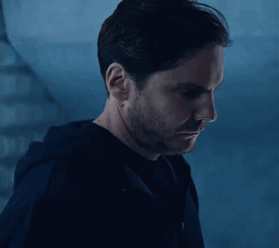 A Man With A Beard And Mustache Is Standing In Front Of A Staircase In A Dark Room . GIF
