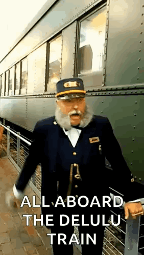 A Man With A Beard And Mustache Is Standing In Front Of A Train With The Words `` All Aboard The Delulu Train '' GIF