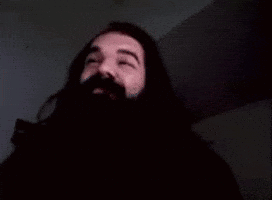 A Man With A Beard And Mustache Is Waving His Hand In The Dark . GIF