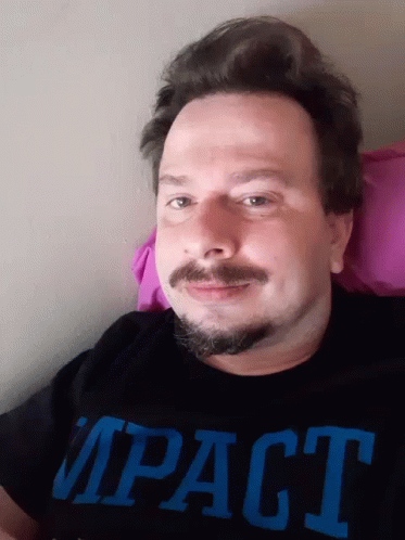 A Man With A Beard And Mustache Is Wearing A Black Impact Shirt GIF