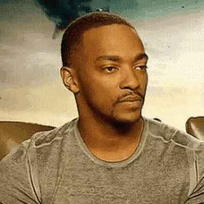 A Man With A Beard And Mustache Is Wearing A Grey Shirt And Looking At The Camera . GIF