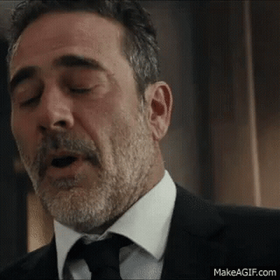 A Man With A Beard And Mustache Is Wearing A Suit And Tie And Yawning . GIF