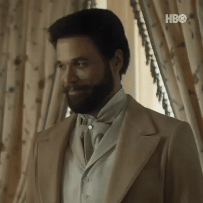 A Man With A Beard And Mustache Is Wearing A Suit And Tie . GIF