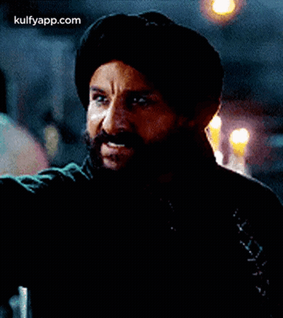 A Man With A Beard And Mustache Is Wearing A Turban And A Black Jacket . GIF