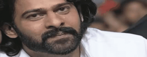 A Man With A Beard And Mustache Is Wearing A White Shirt And Making A Funny Face . GIF