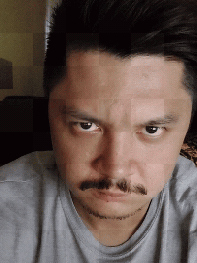 A Man With A Beard And Mustache Looks At The Camera With A Serious Look On His Face GIF