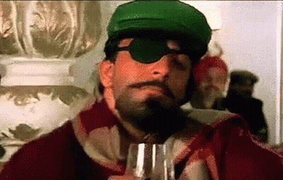 A Man With A Beard And Mustache Wearing A Green Hat And Sunglasses Is Holding A Glass Of Wine . GIF