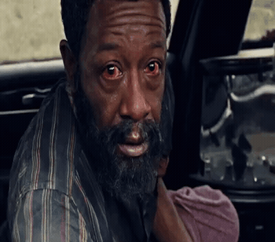 A Man With A Beard And Red Eyes Is Holding A Baby In His Arms . GIF