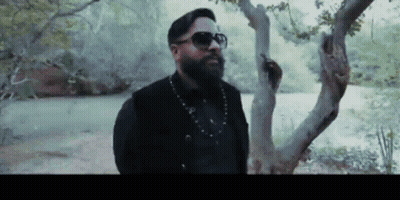 A Man With A Beard And Sunglasses Is Leaning Against A Tree GIF