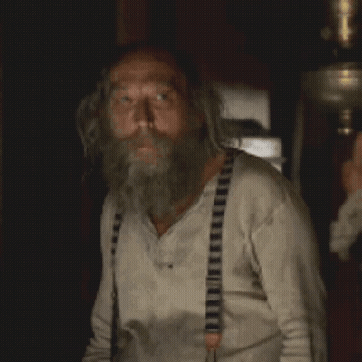 A Man With A Beard And Suspenders Is Looking At Something GIF