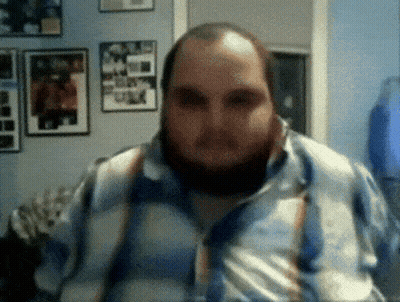 A Man With A Beard And Suspenders Is Looking At The Camera GIF