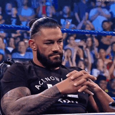 A Man With A Beard And Tattoos Is Sitting In A Chair In A Wrestling Ring . GIF