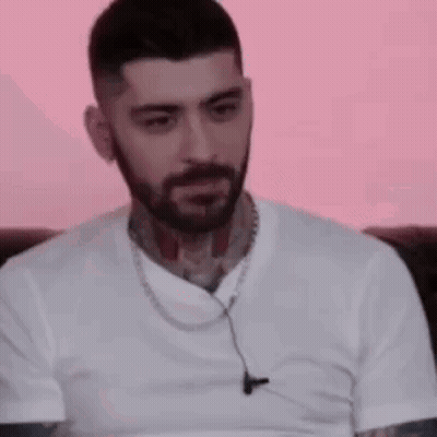 A Man With A Beard And Tattoos Is Wearing A White T-Shirt And Ear Buds . GIF