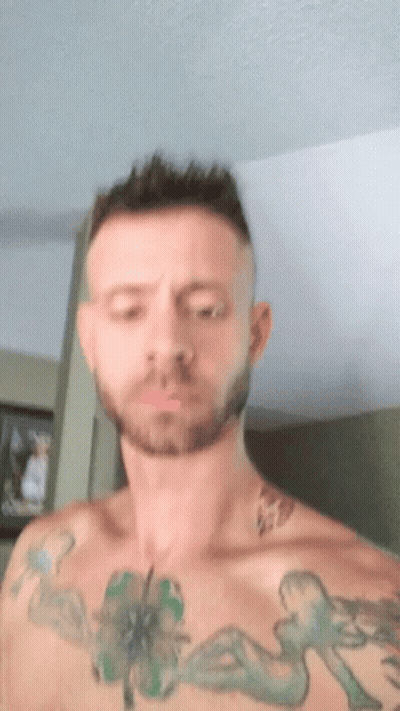 A Man With A Beard And Tattoos On His Chest Is Making A Funny Face . GIF