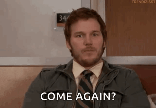 A Man With A Beard And Tie Is Sitting On A Couch And Says Come Again . GIF