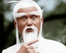 A Man With A Beard And White Hair Is Making A Funny Face And Pointing At Something . GIF