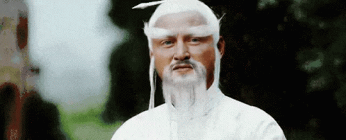 A Man With A Beard And White Hair Is Wearing A White Hat And A White Wig . GIF