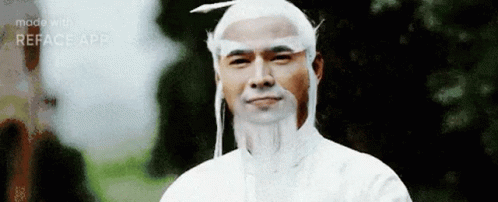 A Man With A Beard And White Hair Is Wearing A White Shirt And A White Hat . GIF