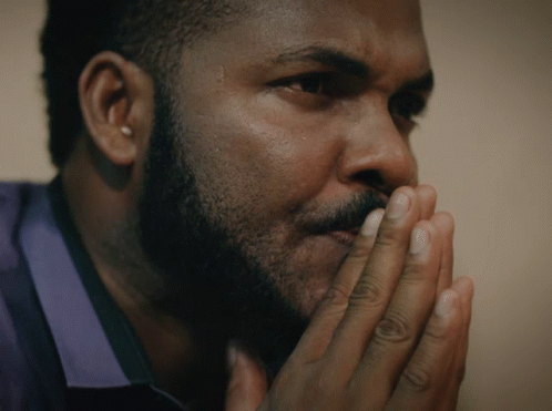 A Man With A Beard Has His Hands Folded In Front Of His Face GIF