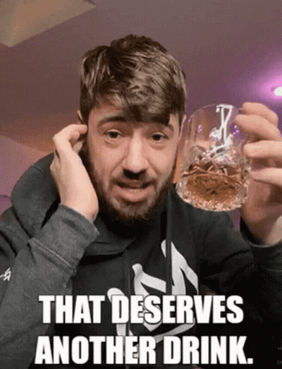 A Man With A Beard Holds A Glass Of Whiskey With The Caption That Deserves Another Drink GIF