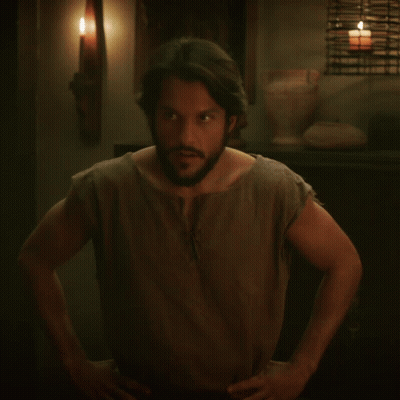 A Man With A Beard Holds His Hand To His Head In A Dark Room GIF