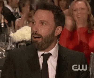 A Man With A Beard In A Suit And Tie Is Sitting In A Crowd Of People . GIF