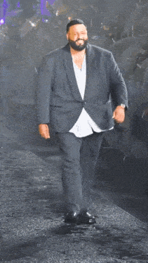 A Man With A Beard In A Suit Is Walking Down A Street GIF
