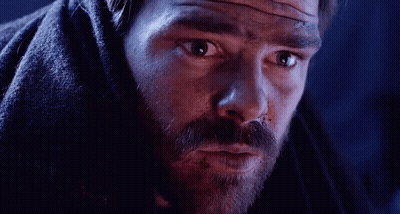 A Man With A Beard Is Covered In A Blanket And Looking At The Camera . GIF