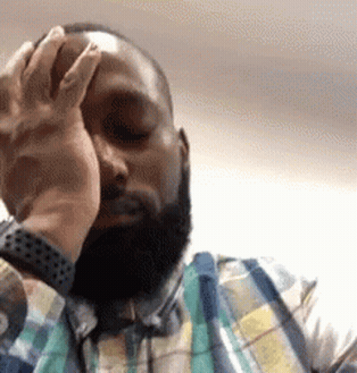 A Man With A Beard Is Covering His Face With His Hand While Wearing A Plaid Shirt . GIF