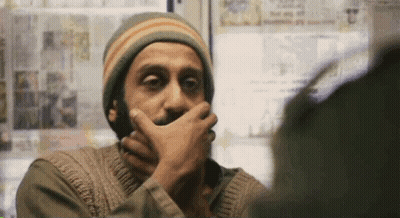 A Man With A Beard Is Covering His Mouth With His Hand While Looking At Another Man . GIF