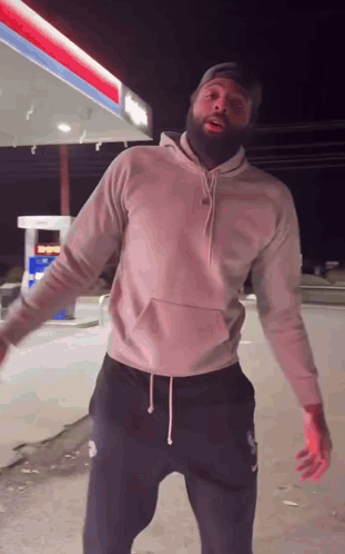 A Man With A Beard Is Dancing In Front Of A Gas Station . GIF