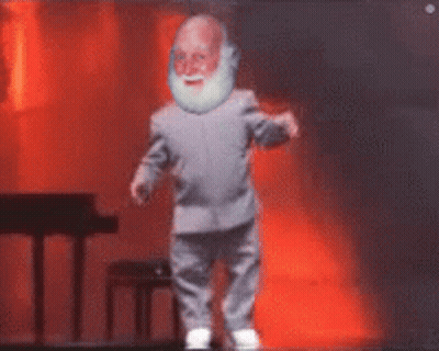 A Man With A Beard Is Dancing On A Stage With A Piano In The Background GIF