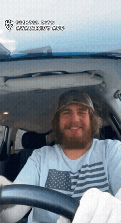 A Man With A Beard Is Driving A Car With The Avatarify App On The Screen GIF