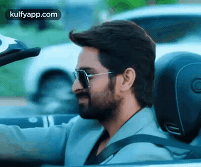 A Man With A Beard Is Driving A Convertible Car With Sunglasses On . GIF