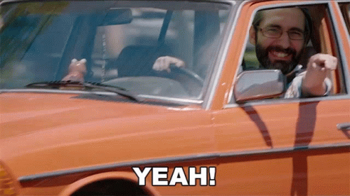 A Man With A Beard Is Driving An Orange Car And Says Yeah GIF