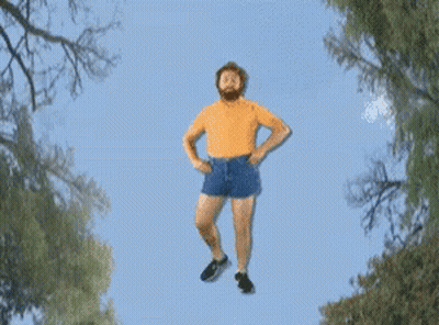 A Man With A Beard Is Flying Through The Air With His Arms Outstretched GIF