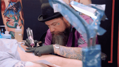 A Man With A Beard Is Getting A Tattoo On A Person 'S Arm GIF