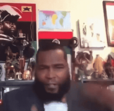 A Man With A Beard Is Giving A Thumbs Up In Front Of A Wall With A Map Of The World On It GIF