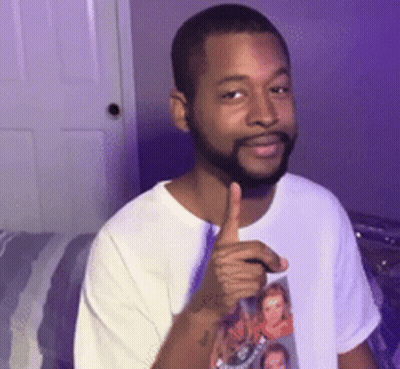 A Man With A Beard Is Giving A Thumbs Up While Wearing A White Shirt With A Picture On It . GIF