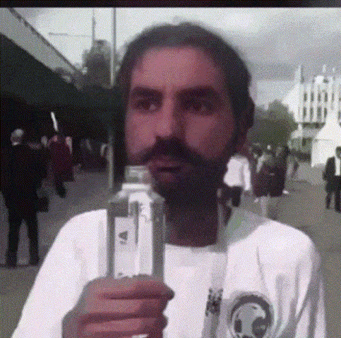 A Man With A Beard Is Holding A Bottle In His Hand GIF