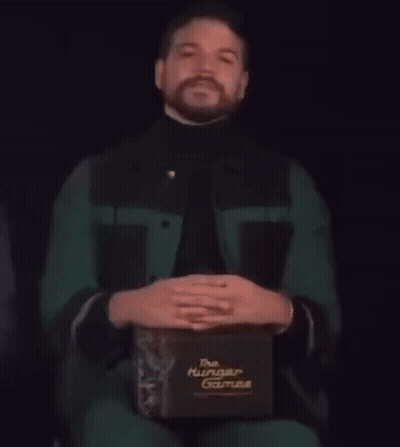 A Man With A Beard Is Holding A Box That Says The Hunger Games GIF