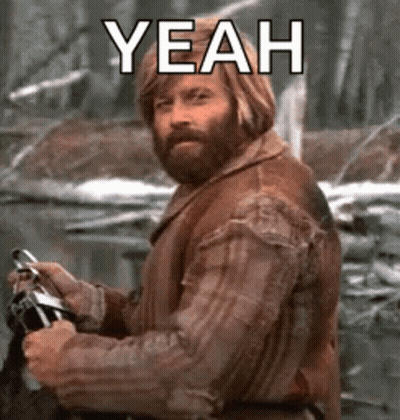 A Man With A Beard Is Holding A Camera And Says `` Yeah '' While Standing In The Woods . GIF