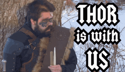 A Man With A Beard Is Holding A Candle In Front Of A Tree With The Words Thor Is With Us Above Him GIF
