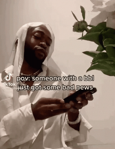 A Man With A Beard Is Holding A Cell Phone In Front Of A Flower . GIF