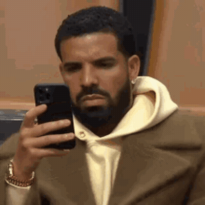 A Man With A Beard Is Holding A Cell Phone In His Hand . GIF