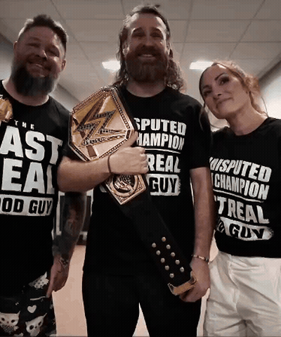 A Man With A Beard Is Holding A Championship Belt Next To Two Other People GIF